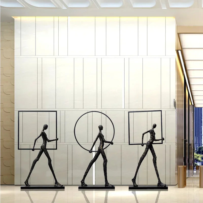 Three abstract bronze human figure sculptures with geometric frames on black bases complement living room home decor