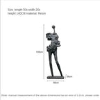 Black resin sculpture of abstract human figure with elongated limbs alongside comforting velvet sofa cushion for living room decor