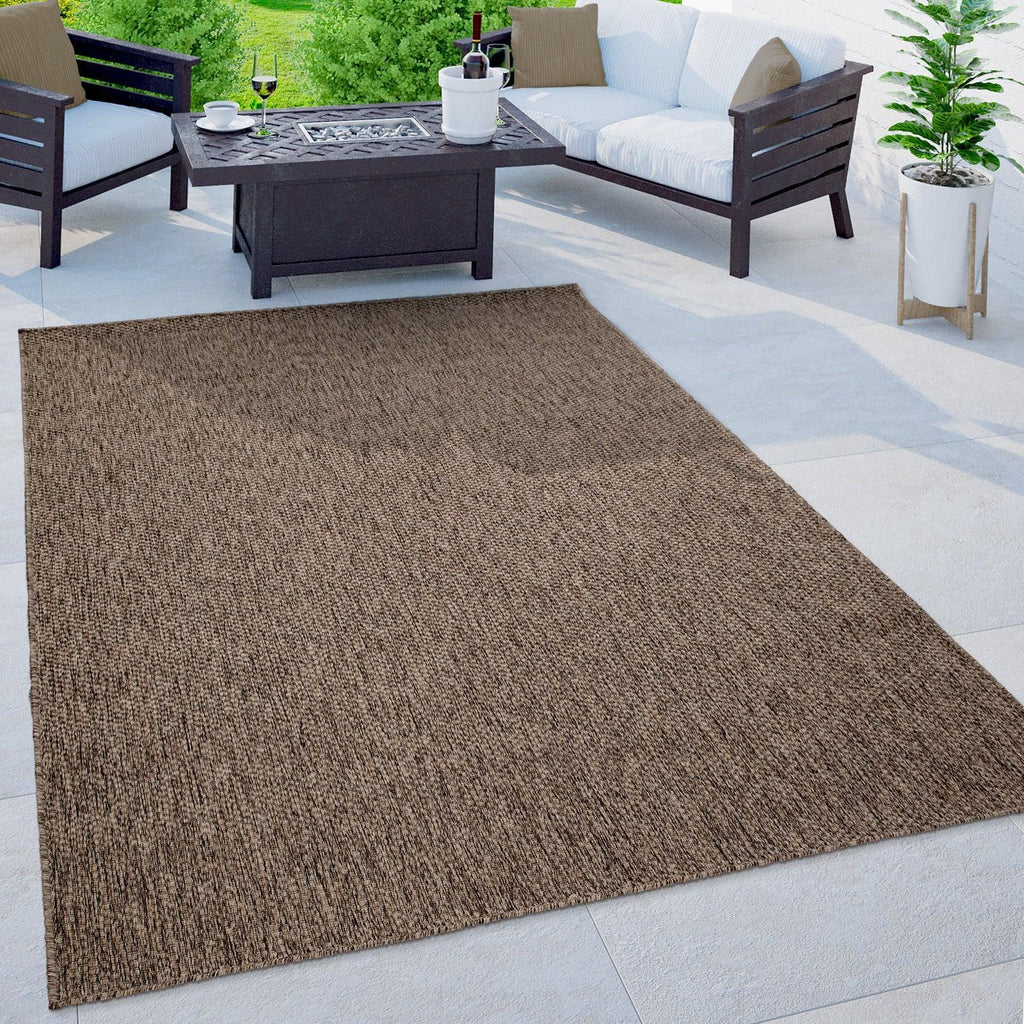 Mottled brown weatherproof outdoor rug placed on a stone patio with modern white and dark wood furniture.