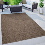 Mottled brown weatherproof outdoor rug placed on a stone patio with modern white and dark wood furniture.