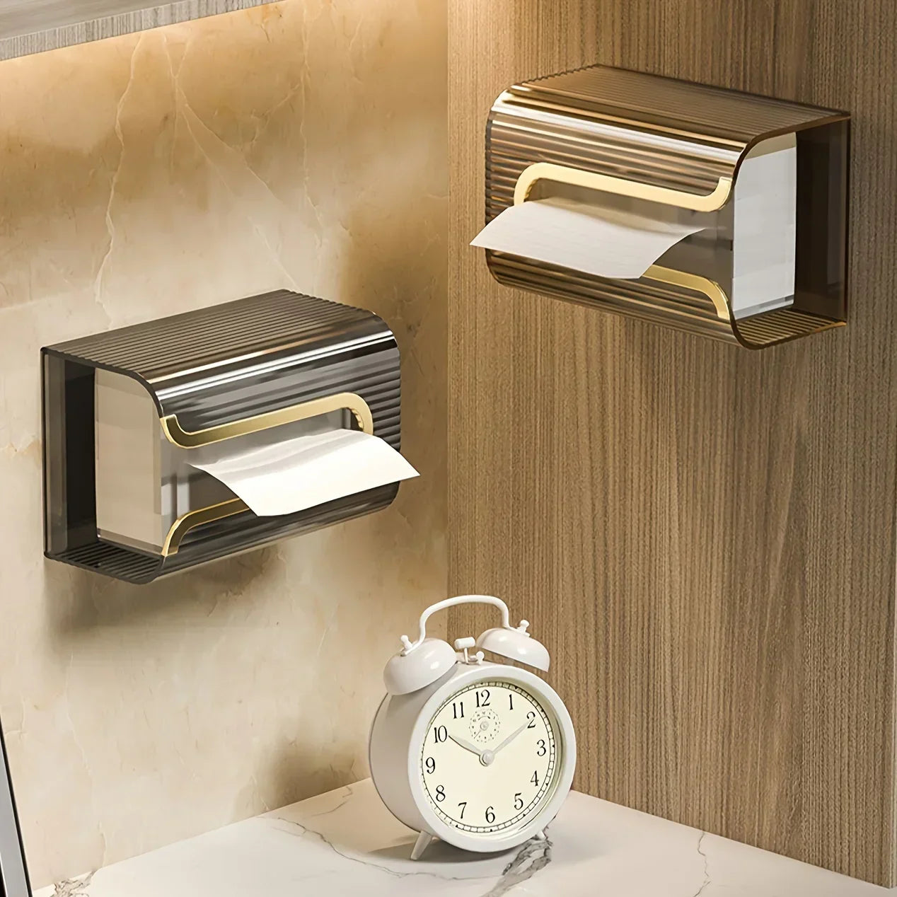 Two gold and black paper towel holders on a wall with a white alarm clock in the foreground.