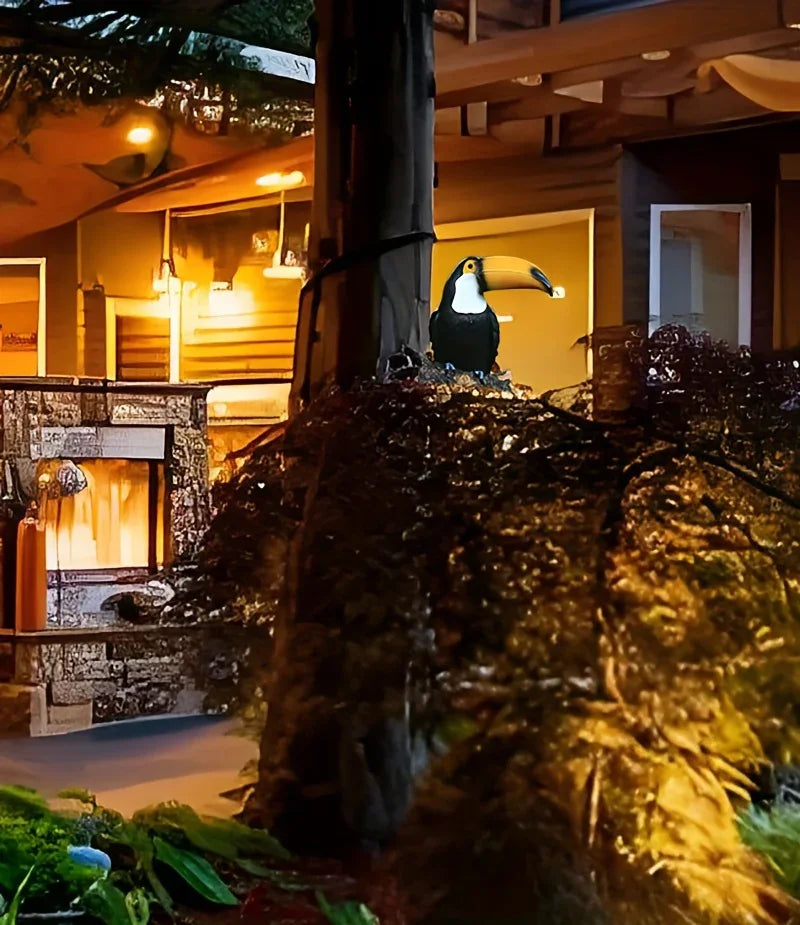Decorative toucan figure on a plant in front of a house with warm lighting