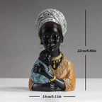 Black resin traditional african mother figurine wearing patterned white headwrap and gold jewelry holding baby in blue fabric