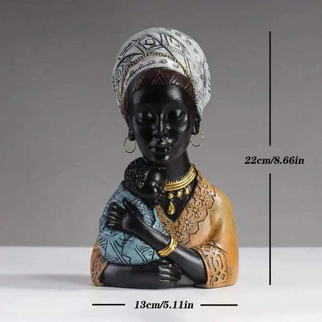 Black resin traditional african mother figurine wearing patterned white headwrap and gold jewelry holding baby in blue fabric