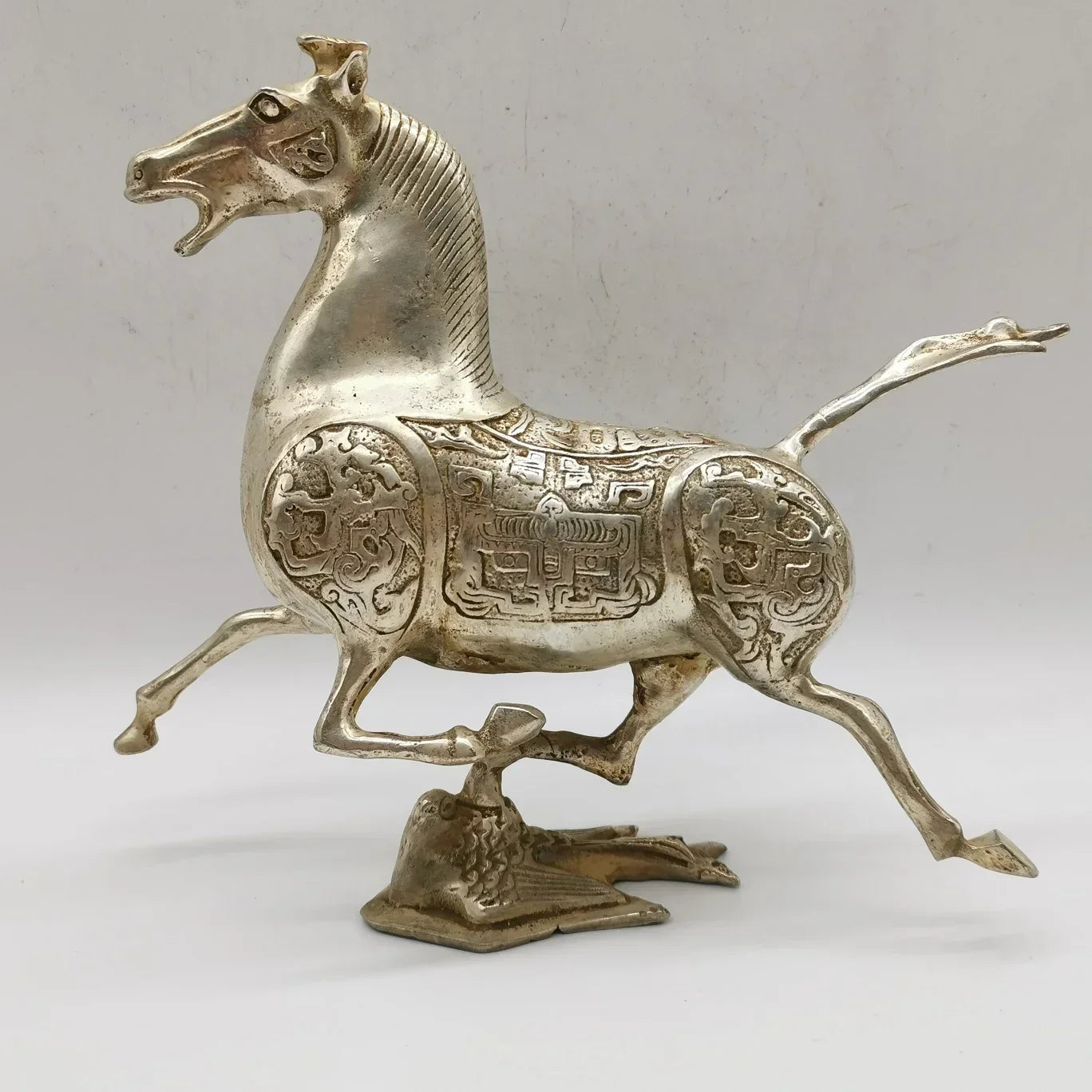 Silver-colored metal horse statue with intricate engraving and detailed saddle on bird-shaped base for vintage bronze decor