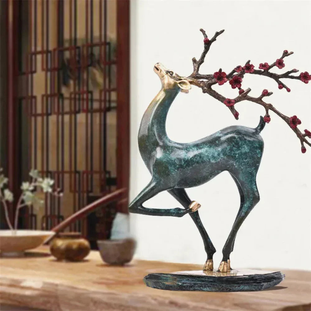 Bronze vintage deer statue with green patina holding a red blossom branch on a dark base for elegant decor