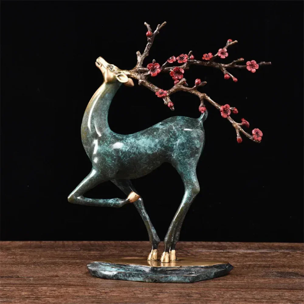 Vintage deer statue in bronze with green patina gracefully carrying a pink blossom branch for elegant decor