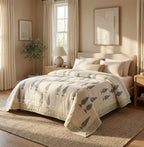 A beige quilted comforter with a gray bird pattern, styled on a bed in a warm, sunlit bedroom with neutral decor. [[SKU:HOA-COM-RUSG-025]]