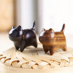 Two wooden cat figurines on a woven surface with a blurred background