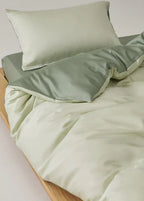 Light green bedding set with a pillow on a wooden bed frame.