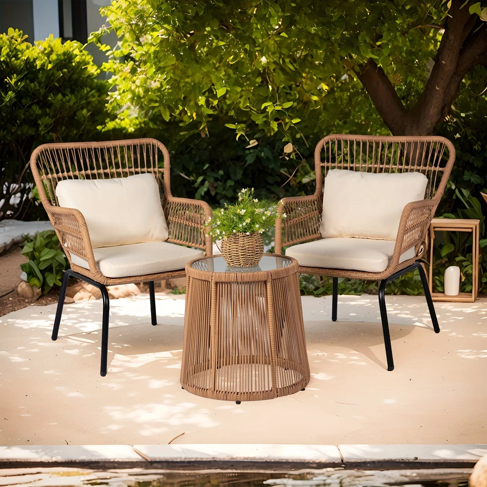 3-piece boho wicker patio furniture set with two beige cushioned armchairs and a round glass-top side table outdoors.