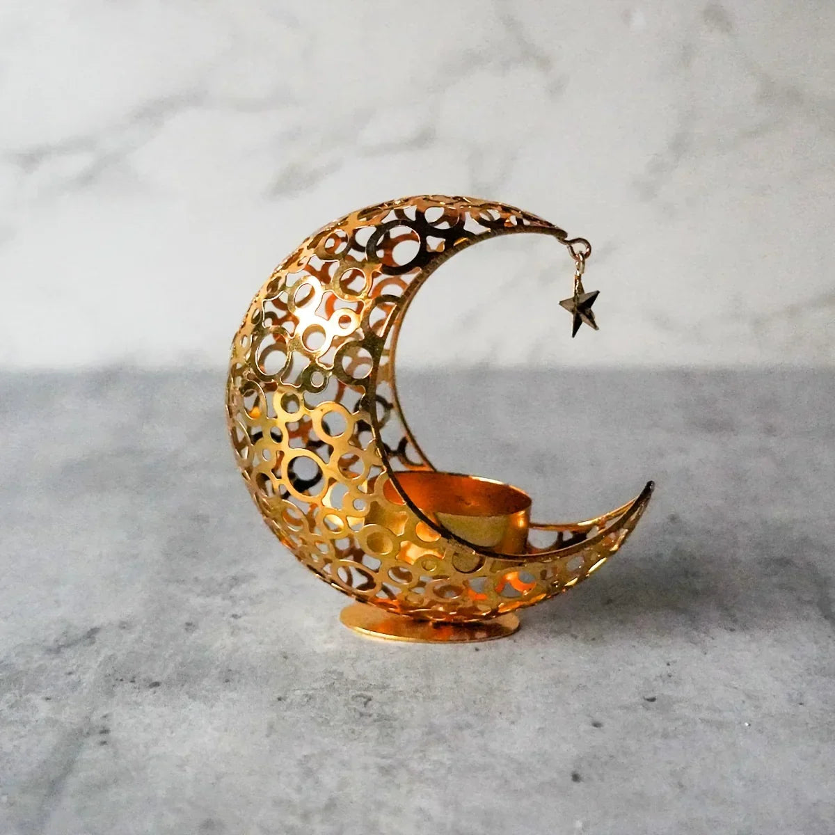 Decorative gold crescent moon and star candle holder on a gray surface