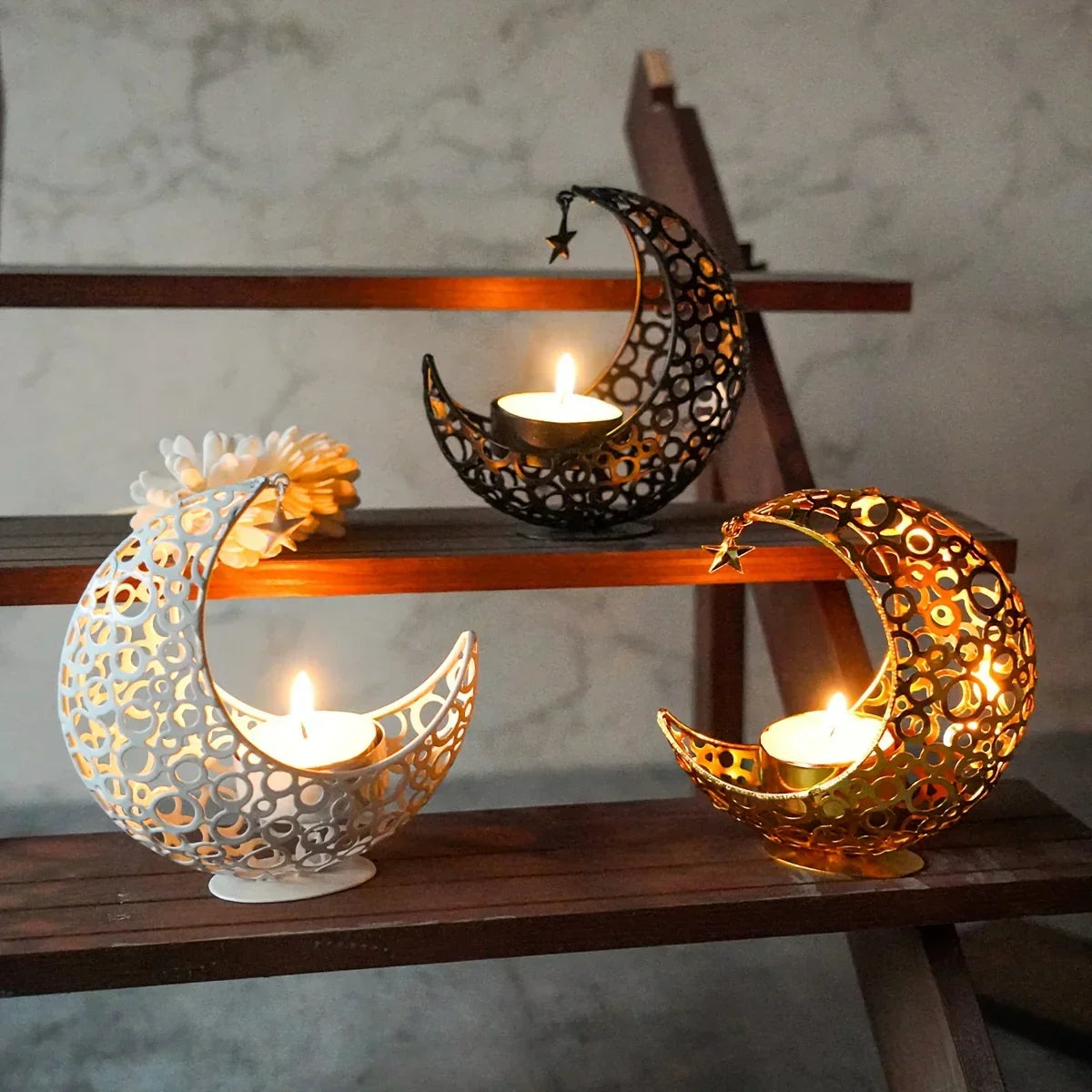 Decorative candle holders shaped like moons on a wooden shelf with a marble wall background.