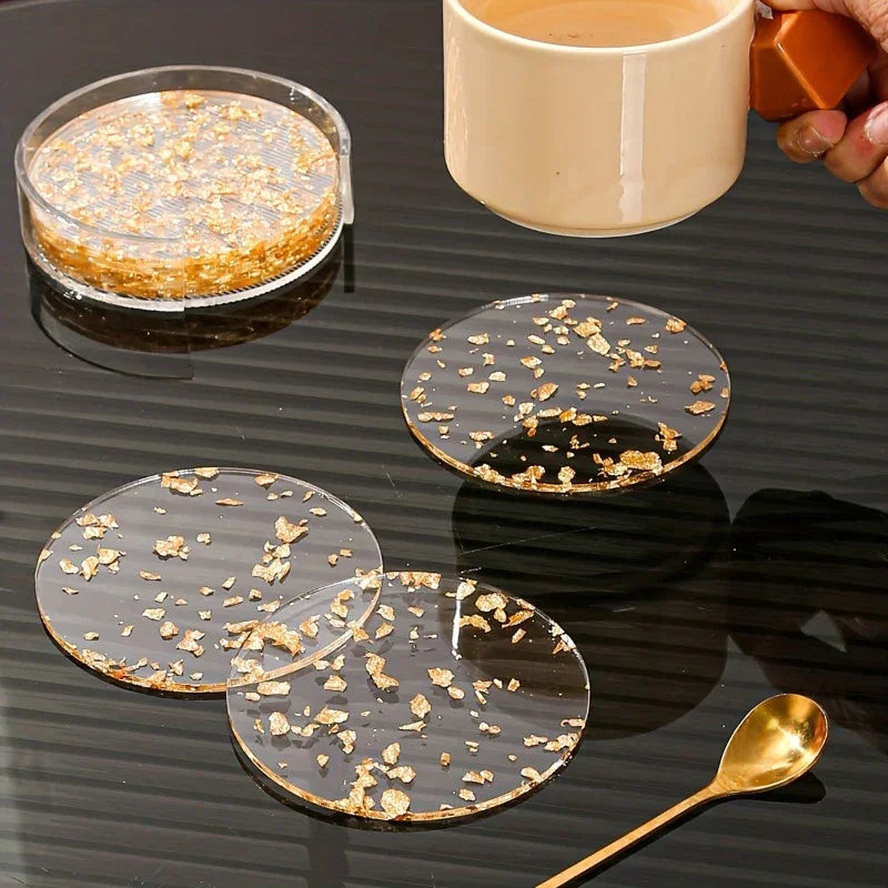 Clear circular acrylic coasters with gold-tone polished metal flakes and a matching holder on a black surface.
