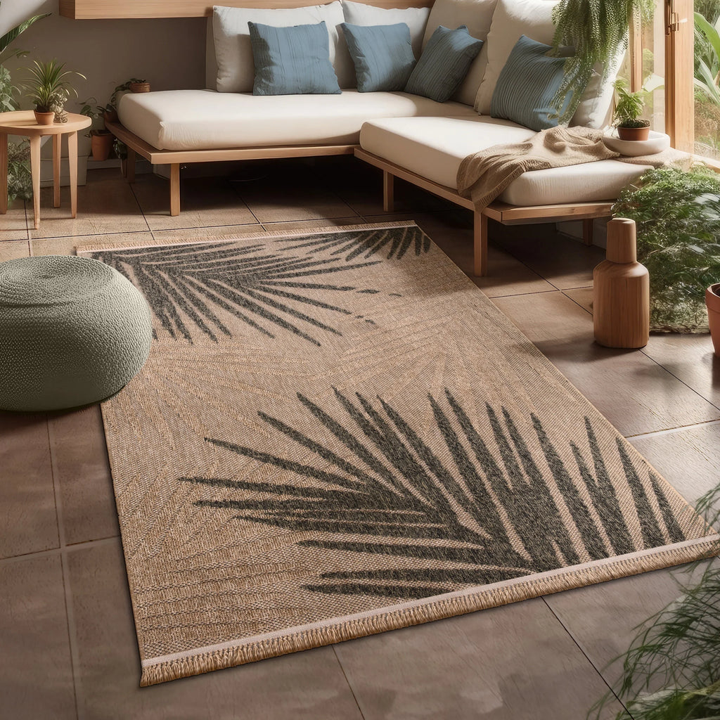 Beige indoor outdoor rug with large dark grey palm leaf design in a modern sunlit room.