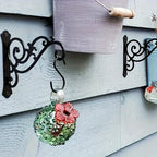 Two black metal decorative swirl wall hooks mounted on a wooden wall holding a bucket and glass ornament. [[SKU:HOA-GDN-003]]