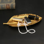 Gold leaf shaped decorative tray holding pearls and lipstick on a dark surface