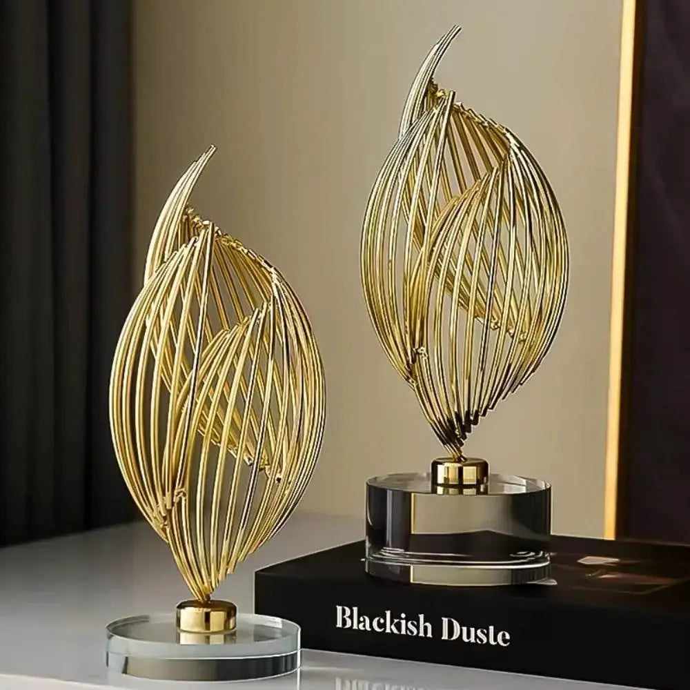 Pair of curved gold wire art ornaments on thick clear acrylic stands, styled on a table with a black book.