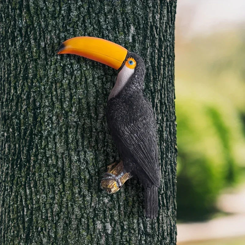 Handcrafted toucan bird sculpture with a yellow beak mounted on a tree trunk for outdoor garden decor.