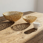 Two decorative gold bowls on a wooden surface with a white mug.