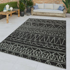 Black and grey outdoor rug with a modern ethnic geometric pattern on a patio with a sofa and plants.