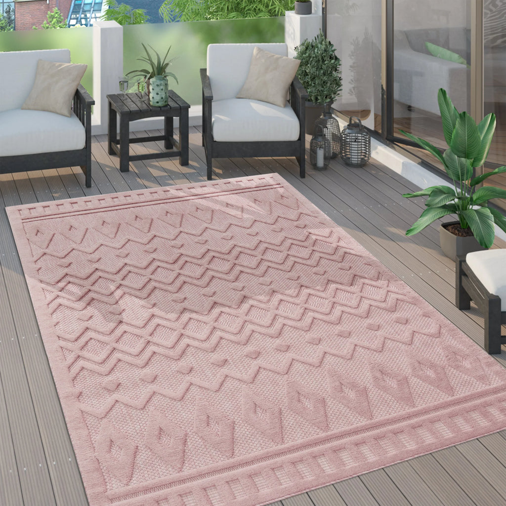 Pink geometric trellis pattern indoor outdoor rug on a modern wooden patio deck with white chairs.