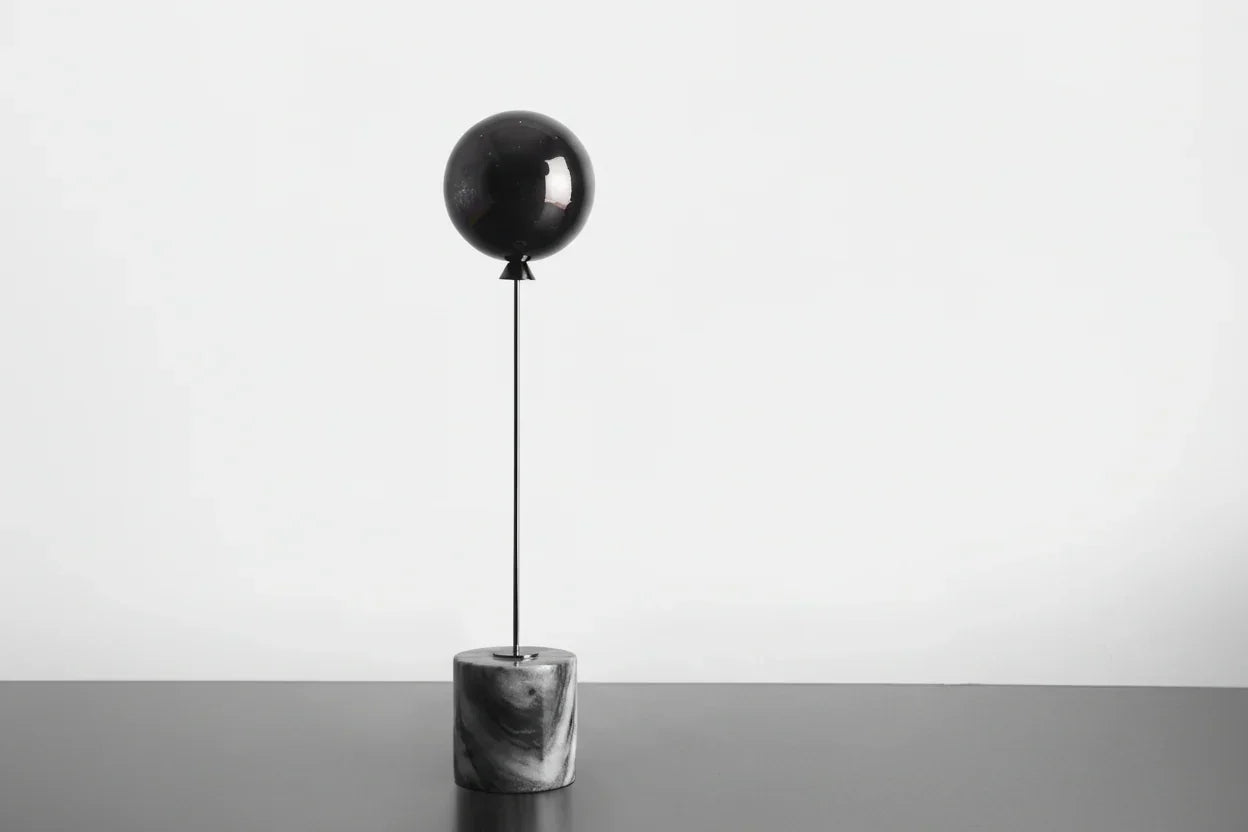 Decorative object with a black sphere and marble base on a white background