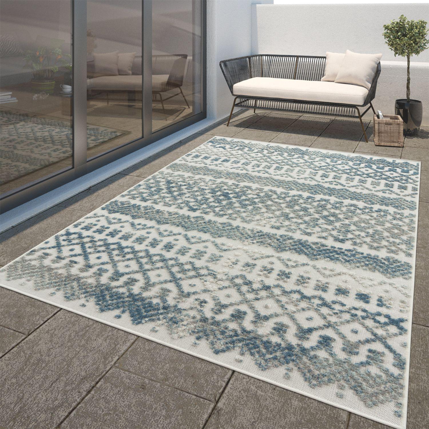 Turquoise and cream Marrakesh high-low trellis pattern rug on a stone patio with outdoor furniture.