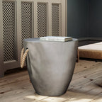 Modern light gray drum-shaped end table with rope handles and a faux slate top in a home setting.