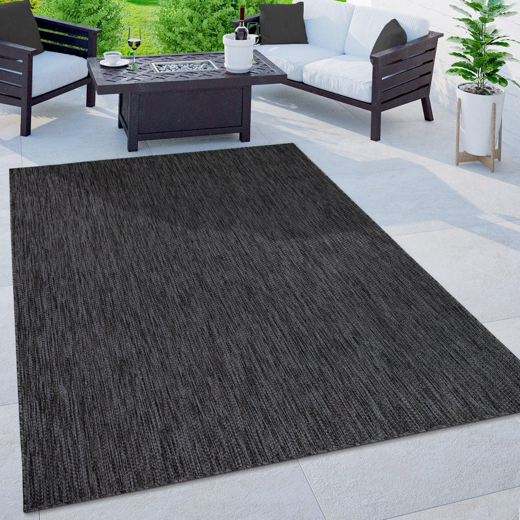 Mottled anthracite outdoor rug on a modern patio with dark furniture and a fire pit table.