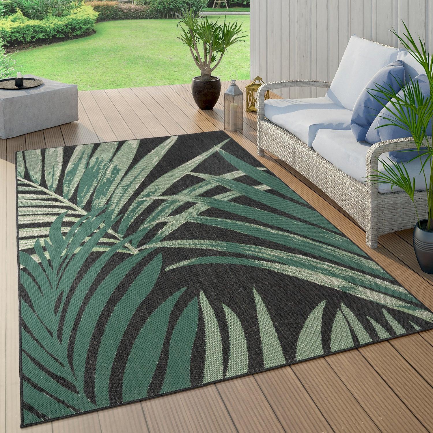 Tropical outdoor rug with large green palm leaves on a black background on a wooden deck.