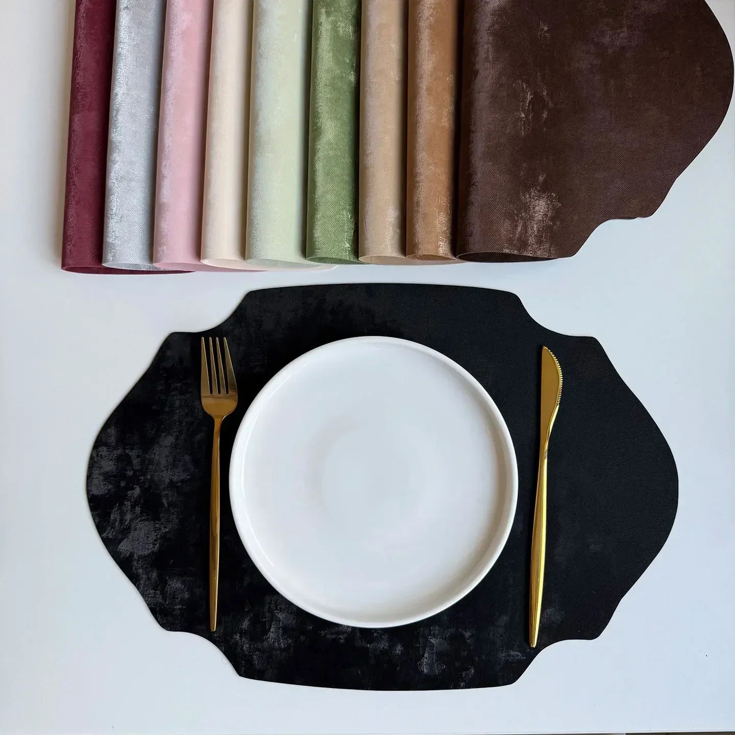 Black scalloped placemat with a white plate, gold fork, and knife on a light gray background.