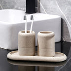 Beige textured bathroom accessory set with two tumblers and an oval tray holding toothbrushes by a white sink.