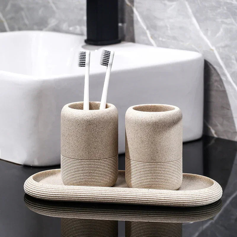 Beige textured bathroom accessory set with two tumblers and an oval tray holding toothbrushes by a white sink.