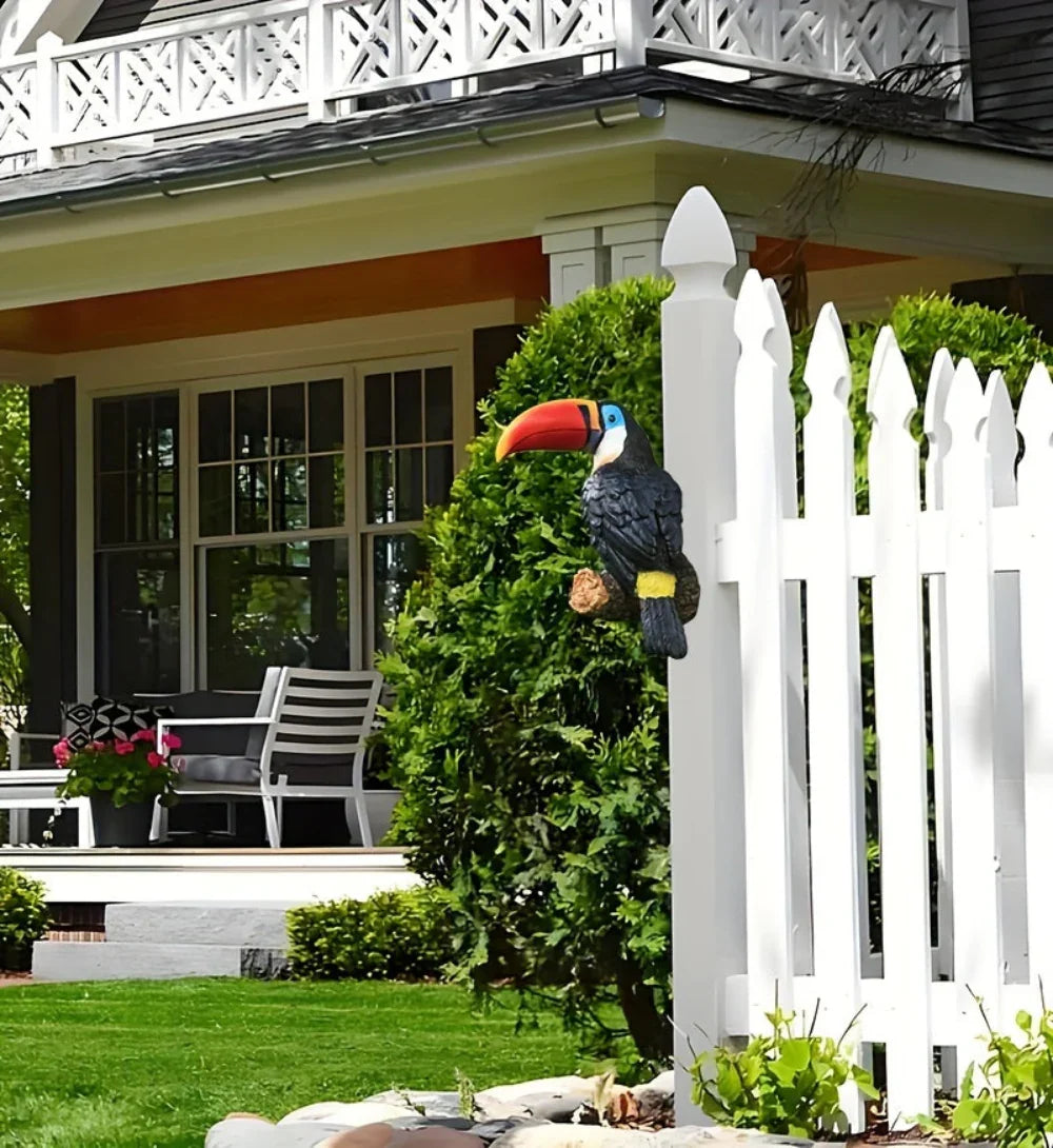Decorative toucan sculpture on a white picket fence in front of a house with a porch.