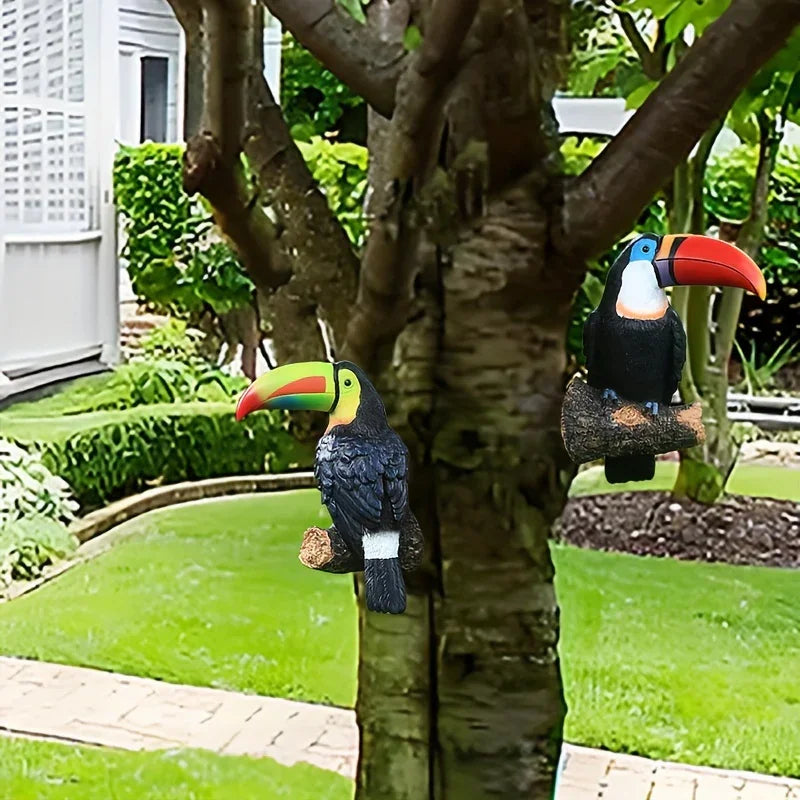 Two toucan figurines perched on tree branches in a garden setting.