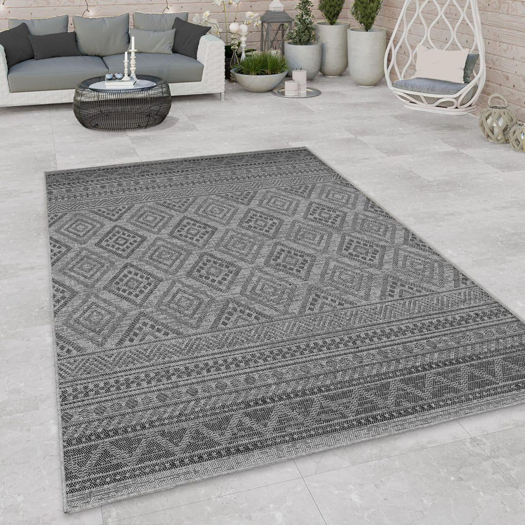 Dark grey outdoor rug with a geometric boho diamond pattern on a modern stone patio.