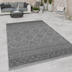 Dark grey outdoor rug with a geometric boho diamond pattern on a modern stone patio.