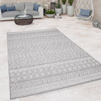 Grey boho outdoor rug with geometric pattern on a stone patio with modern outdoor furniture.