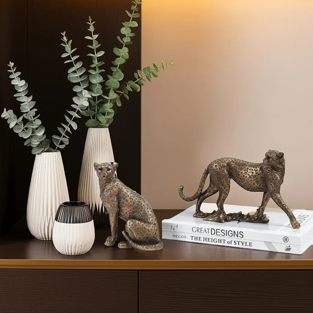 Decorative items including a vase with greenery, two cat figurines, and a book titled 'Great Designs' on a wooden surface.