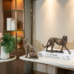 Two bronze cat sculptures on books with a decorative setting