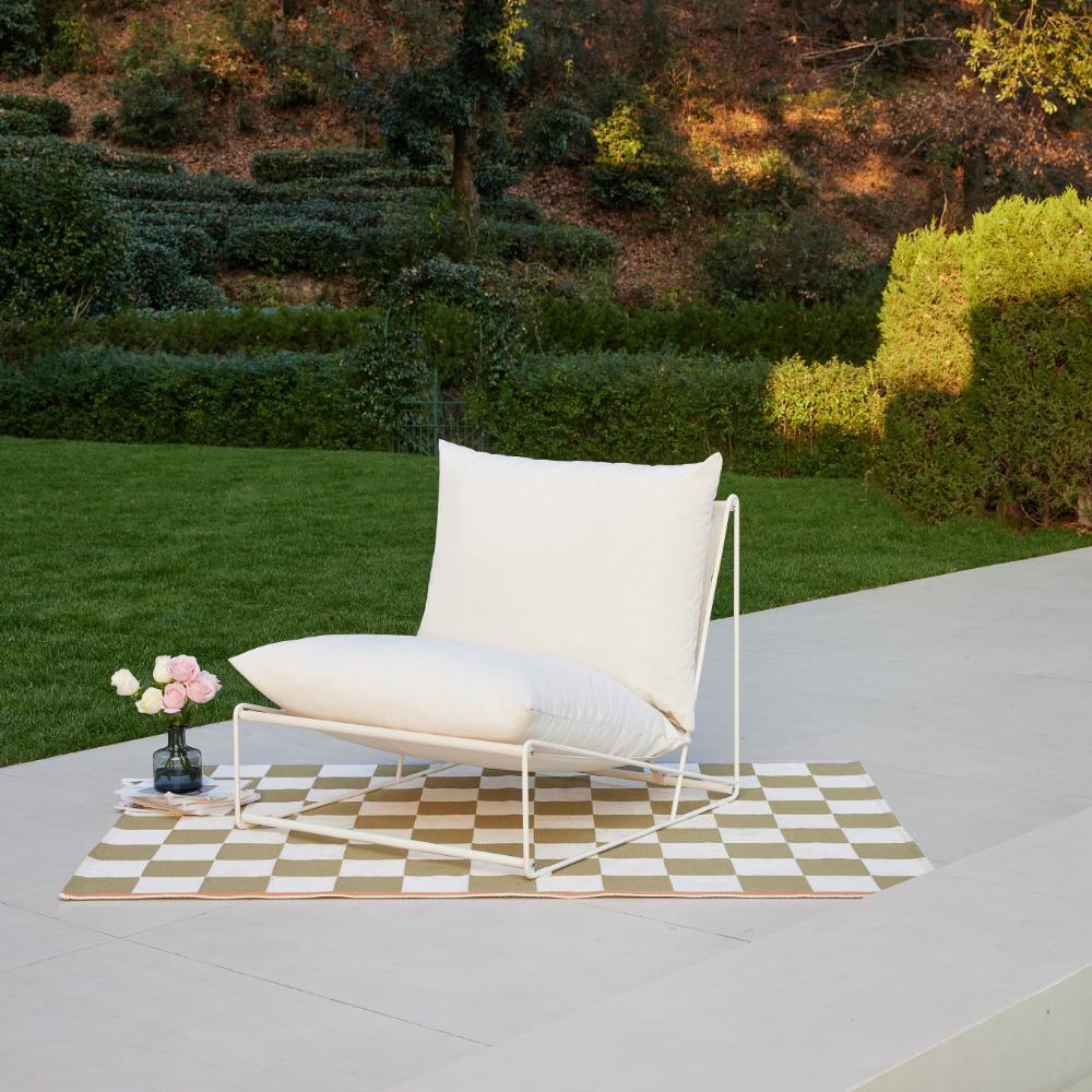 Modern white aluminum garden chair with plush white cushions on a patio overlooking a lush green garden.