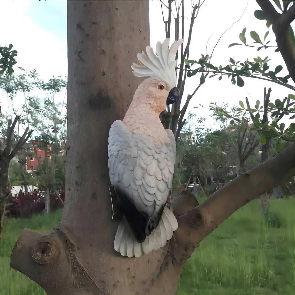 Lifelike white and pink parrot sculpture mounted on a tree trunk in a lush garden.