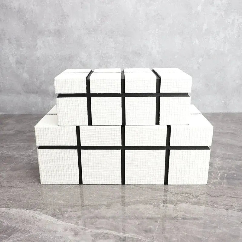 Stacked white textured boxes with black geometric accents complement a modern matte black thinker sculpture figurine
