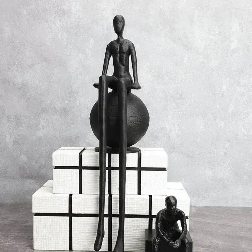 Black abstract thinker sculpture with elongated limbs seated on a modern matte black spherical base figurine