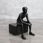 Matte black thinker sculpture of a seated human form with smooth contours on a modern matte black cube base