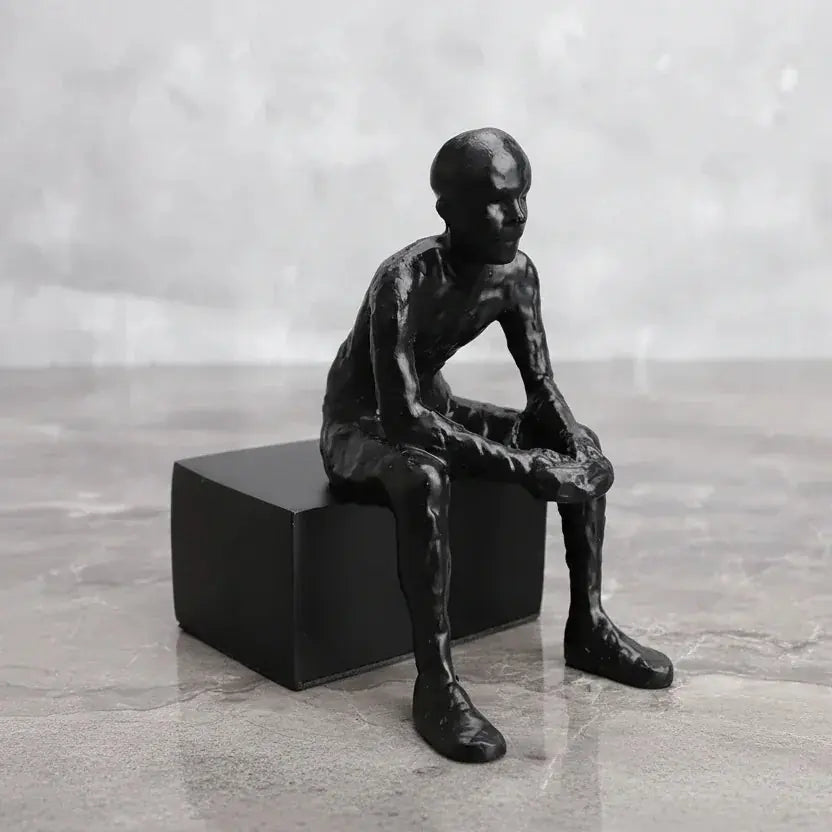 Matte black thinker sculpture of a seated human form with smooth contours on a modern matte black cube base