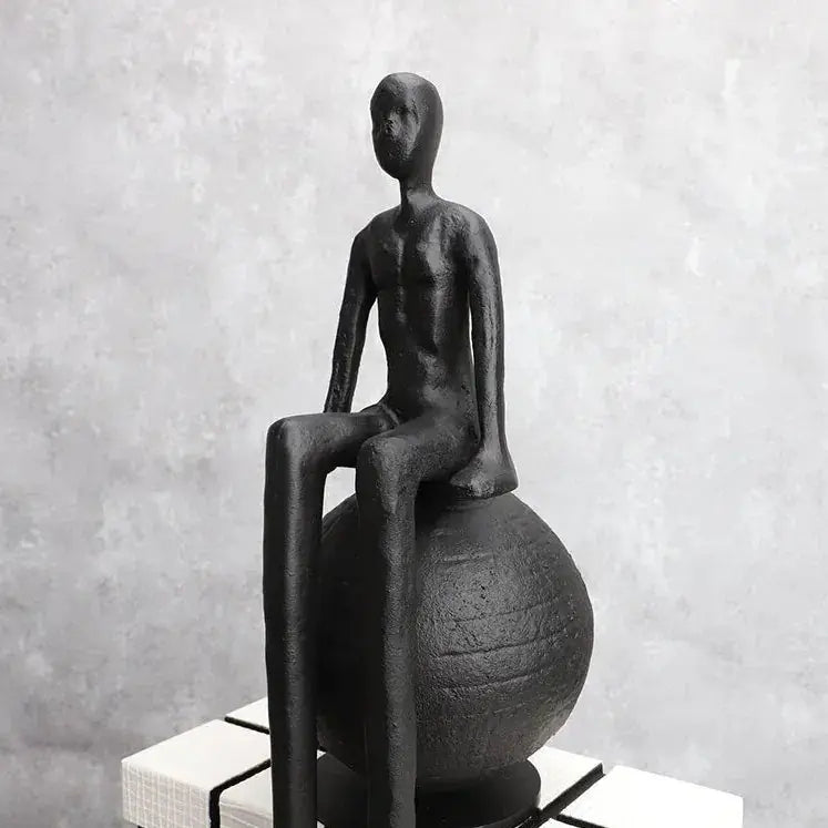 Abstract long-legged thinker sculpture in modern matte black finish seated on a textured spherical base