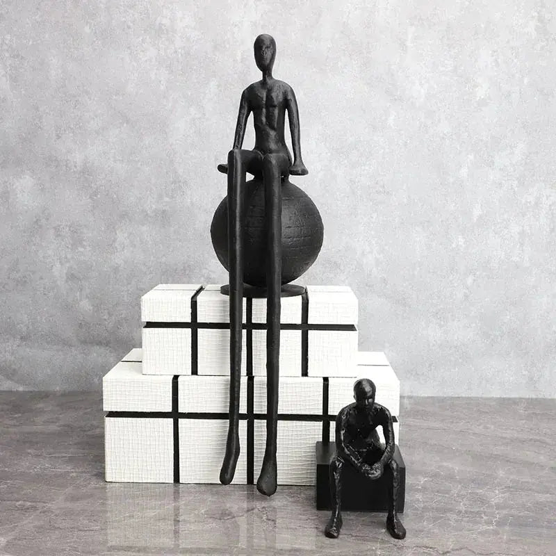 Abstract long-legged thinker sculpture featuring a modern matte black finish on a seated figure atop a spherical base