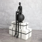 Modern matte black thinker sculpture with elongated limbs seated atop a textured matte black sphere